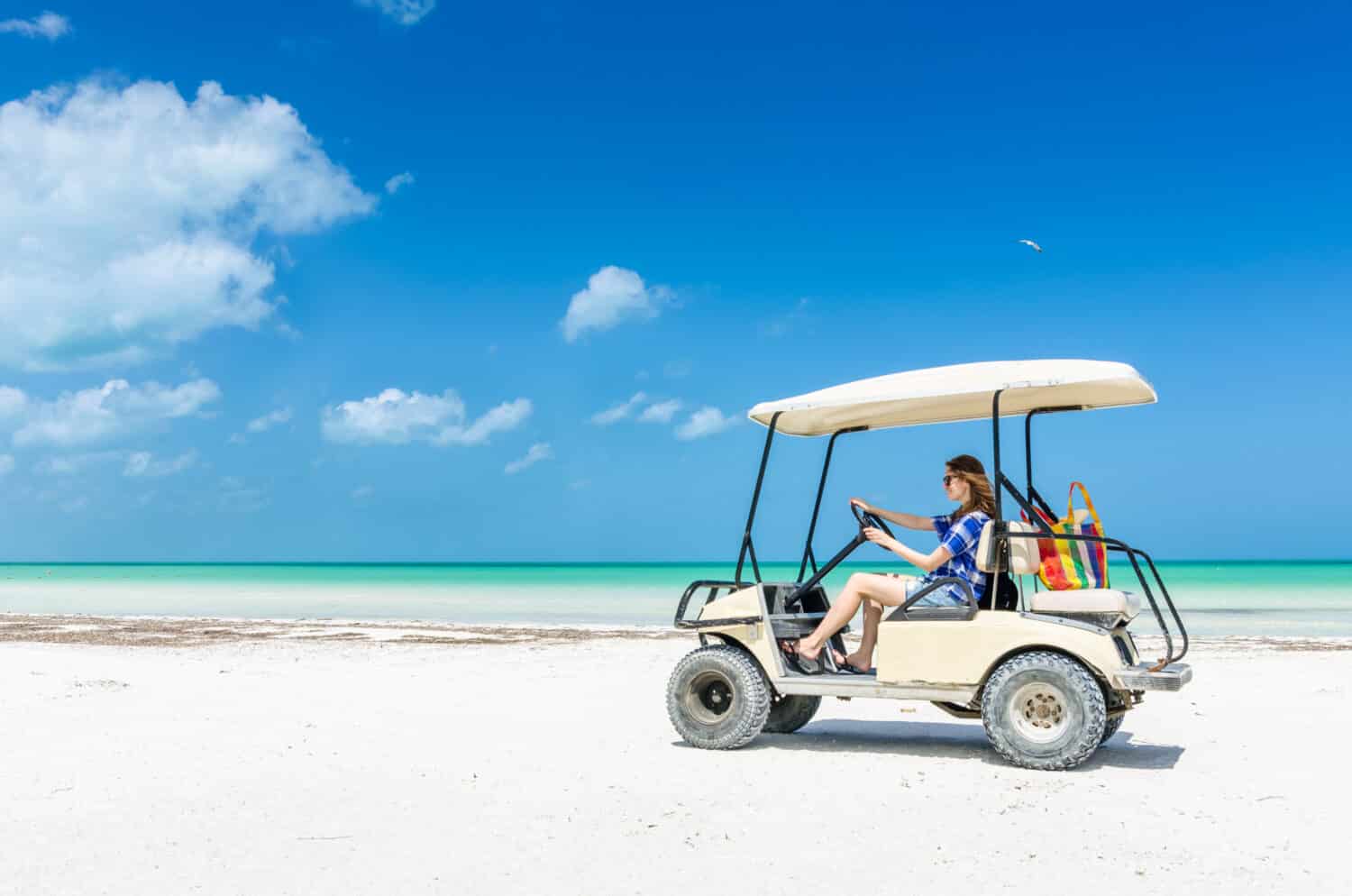 Young woman driving golf cart along tropical sandy beach